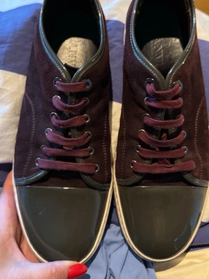 Lanvin DBB1 cap toe sneakers  - Snygga vinröda och gröna sneakers med ovandel i mocka och matchande vinröda skosnören. Tåpartiet är i blankt grönt lackmaterial och kanten runt öppningen har en grå detalj. Yttersulan är ljus och ger en fräsch kontrast. Perfekta för dig som gillar stilrena detaljer. Någon liten repa på den lackade delen, se bilder. 