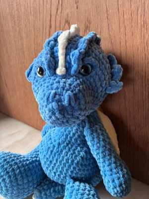 Virkad drake - Blå drake som är virkad i mjukt garn. Storlek större. Draken har vita detaljer på ryggen och huvudet samt säkerhetsögon. Perfekt som prydnad eller kramkompis. 
