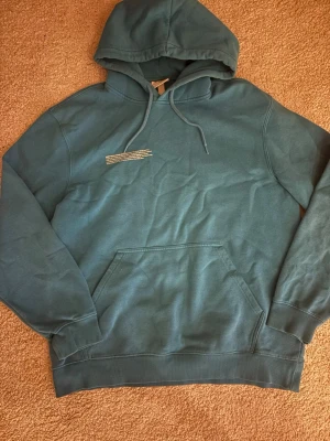 Blå hoodie från H&M med tryck - Snygg blå hoodie från H&M i regular fit med huva och dragsko. Framtill finns en liten vit textdetalj och en klassisk känguruficka. Perfekt för en avslappnad och cool stil. Tillverkad i mjuk bomullsblandning. Den sitter som en Medel/ large om ni vill ha mått så är det bara att skriva😁