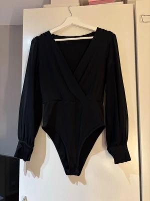 Svart omlott body med v-ringning - Svart blus med body och djup v-ringning. Storlek är okänt men skulle säga S, från HM. Långa armar i transparent material. Riktigt bra passform och fin till middagar eller andra fintillfällen.