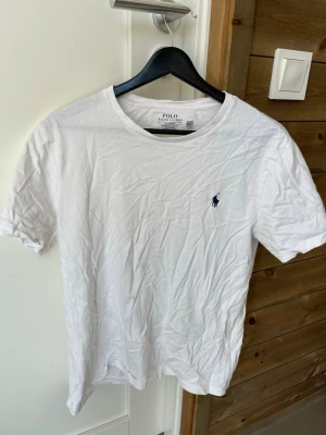 Vit t-shirt från Polo Ralph Lauren - Klassisk vit t-shirt från Polo Ralph Lauren med rund hals och liten broderad logga på bröstet. Modellen är slim fit och tillverkad i mjuk bomull, perfekt för en clean och stilren look.