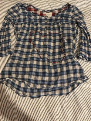 Blårutig blus med broderi och knappar - Söt blus i blåvitt rutigt mönster med broderade detaljer vid axlarna och små knappar framtill. Blusen har trekvartsärmar och en avslappnad passform. Materialet känns lätt och luftigt, perfekt för vår och sommar.