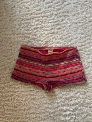 Randiga shorts i rosa och orange toner - Färgglada shorts med horisontella ränder i rosa, orange, röd och lila. De har en tight passform och är tillverkade i ett mjukt, stretchigt material. Perfekta för sommardagar när du vill sticka ut lite extra.