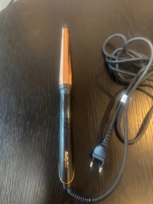  locktång från BaByliss - Säljer en konformad locktång från BaByliss med svart handtag och kopparfärgad stav. Utrustad med sladd och europeisk kontakt. Perfekt för att skapa snygga lockar och vågor. Materialet är en kombination av plast och metall.