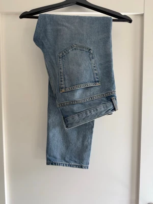 Ljusblå raka jeans med stor ficka - Säljer ett par ljusblå jeans med rak passform och en stor bakficka. Jeansen har klassisk femficksdesign och är gjorda i kraftigt denimtyg. Perfekta för en avslappnad och trendig look.