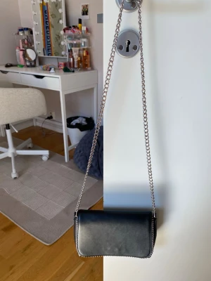 Svart kuvertväska i konstläder - Stilren svart kuvertväska i slätt konstläder med magnetlås och silverfärgade detaljer. Väskan har en enkel, rektangulär form och insidan är fodrad i svart tyg. Perfekt för att bära det viktigaste till utekvällen.