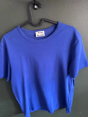 Blå t-shirt från Acne Studios - Säljer en enkel och stilren blå t-shirt från Acne Studios. T-shirten har rund halsringning och korta ärmar. Tillverkad i mjuk bomull som känns skön mot huden. Perfekt basplagg för alla tillfällen.