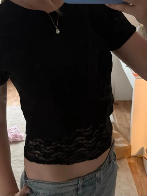 Svart croppad topp med spetskant - Snygg svart croppad topp med korta ärmar och spetsdetalj längst ner. Går att styla separat om man vill. Knappt använd