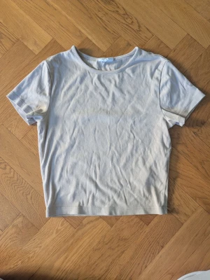 Ljusbeige basic t-shirt - En enkel och stilren ljusbeige t-shirt med rund hals och korta ärmar. Perfekt till jeans eller shorts för en clean och avslappnad look. Tillverkad i mjuk bomull som känns skön mot huden.