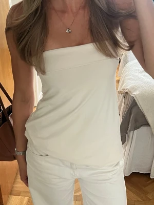 Vit axelbandslös tubtopp - Säljer en stilren vit tubtopp med bandeau-modell. Toppen är ärmlös och har en enkel, clean design som passar perfekt till både jeans och kjol. Tillverkad i mjukt material som sitter bekvämt mot kroppen. Perfekt för varma dagar eller lager på lager.