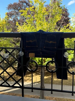 Mörkblå jeans från Nudie Jeans - Säljer ett par mörkblå jeans från Nudie Jeans med klassisk femficksmodell och kontrastsömmar. Jeansen har raka ben och tydliga broderade detaljer på bakfickorna. Materialet är kraftig denim i bomull. Storlek W31 L30