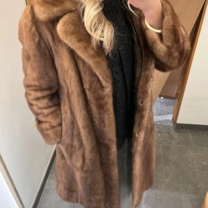 Brun pälsjacka från Saga - Elegant brun pälsjacka från Saga, tillverkad av mink från Skandinavien. Jackan har en klassisk design med långa ärmar och en mjuk, lyxig känsla. Perfekt för att hålla sig varm och stilfull under de kallare månaderna.