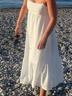 Vit sommarklänning med broderi - Söt vit klänning med smala axelband och broderade detaljer. Klänningen har en luftig passform, volang nedtill och är tillverkad i ett lätt material som passar perfekt för varma dagar.