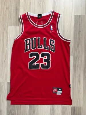 Baskettröja  - Rött basketlinne nummer 23 på både fram- och baksidan. På ryggen står det 'Jordan' och linnet har vita och svarta detaljer vid krage och ärmhål. Perfekt för basket eller streetwear.