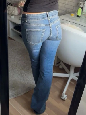 Low waist jeans  - Säljer ett par blå bootcut jeans med låg midja och markerade sömmar framtill. Jeansen har stora fickor både fram och bak samt klassisk knappgylf. Perfekta för en avslappnad och trendig look.