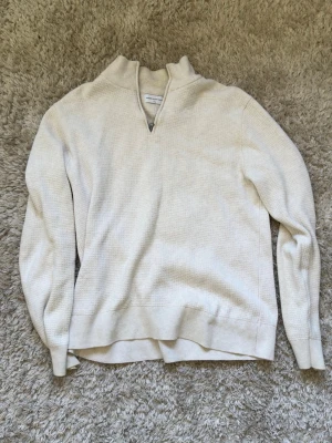 Vit stickad halvzip tröja - Säljer en stilren vit stickad tröja med halvzip och hög krage från These Glory Days. Tröjan har lång ärm och ribbade muddar vid ärmslut och nederkant. Perfekt för lager på lager och enkel att matcha med jeans eller byxor. 