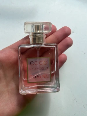 Coco Mademoiselle parfym från Chanel - Coco Mademoiselle parfym från Chanel i en elegant, fyrkantig glasflaska med guld- och transparent kork. Doften är ikonisk och flaskan har en ljusrosa tonad vätska. Perfekt för dig som gillar lyxiga och klassiska parfymer.