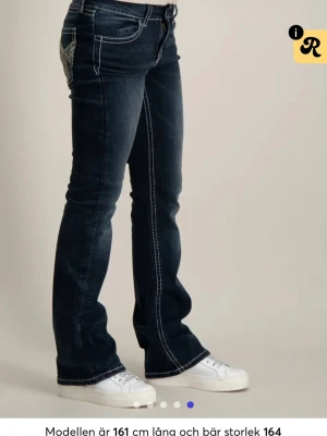 Mörkblå low flare jeans - 💓 Helt nya Gina Tricot Young-jeans i storlek 170! 💓  Säljer dessa då jag fick ett par i dubblett. De är helt oöppnade och ligger fortfarande i originalplastpåsen från beställningen, med lappen kvar.  Mörka bootcut-jeans med låg midja, tight passform upptill och utsvängda ben. Justerbar midja på insidan för extra bra passform. Bakfickorna har fina detaljer med brodyr och paljetter. 💓
