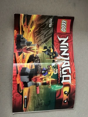LEGO Ninjago 70753 byggdelar & manual - LEGO Ninjago 70753 med byggmanual och blandade klossar i färger som orange, röd och grå. Delarna levereras i en genomskinlig IKEA-påse med guldfärgade blad. Perfekt för dig som gillar att bygga och samla Ninjago.