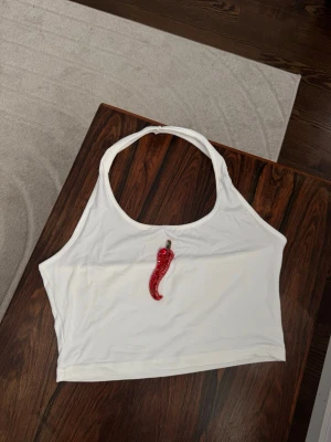 Vit croppad halterneck topp med chili - Säljer en vit croppad halterneck topp med en broderad och glittrig röd chili på bröstet. Patchen är fäst med textillim 🌶️🖤