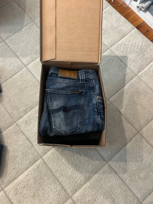 6x nudie jeans  - Säljer ett par klassiska blå jeans från Nudie Jeans med snygg slitning och kontrastsömmar. Jeansen har fem fickor, normal midja och raka ben. Tillverkade i slitstarkt denim med en cool tvättad look.