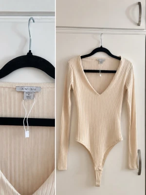 🤍 Beige ribbad body – AMISU – strl S - Snygg beige/cremefärgad ribbad body från AMISU i storlek S 🤍  * Lång ärm * Figurnära modell * Stretchigt ribbat material * Djup V-ringning * Väldigt fin att styla med jeans, kostymbyxor eller kjol ✨  Använd men i fint skick. Säljes då den inte kommer till användning längre.