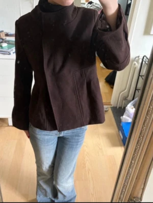 Mörkbrun ulljacka med knappar - Snygg mörkbrun jacka i ull med bred krage från Åhléns. Storlek XS.