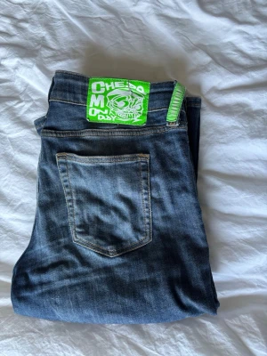 Blå jeans med grön CHEAP MONDAY-detalj - Säljer ett par blå jeans från Cheap Monday. Jätte bekväma med stretchigt tyg. Har ett väldigt litet hål vid låret som inte syns.