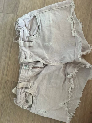 Ljusrosa jeansshorts - Säljer ett par ljusrosa populära shorts från Gina tricot med fransar där nere, dragkedja, knapp och stilrena fickor.