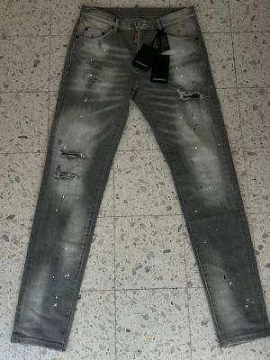 Dsquared2 Jeans med slitningar och färgstänk gråa - Snygga Dsquared jeans i storlek 30. Riktigt fet modell som passar till allt. Jeansen sitter slim. Fraktar inom 0-1 dagar!