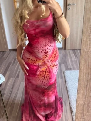 Rosa långklänning med blommönster - Säljer en lång, figurnära klänning i rosa och röda toner med blommigt mönster. Klänningen har smala axelband, öppen rygg och är ärmlös. Materialet ser ut att vara mjukt och stretchigt, perfekt för sommaren.