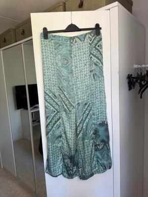 Grön/ blåa byxor  med paisleymönster - Säljer en flowy grön/blåa byxor med paisley- och småblommigt mönster i olika gröna nyanser. Kjolen har en avslappnad passform och är tillverkad i ett mjukt, lätt material som känns svalt och skönt. Perfekt för dig som gillar boho-vibbar och unika prints. Från märket Odd Molly i storlek 3 som enligt deras storlekguide motsvarar en storlek L. Kanske kan vara något små. Mycket fint skick, jag hittar inga synliga anmärkningar eller defekter. 