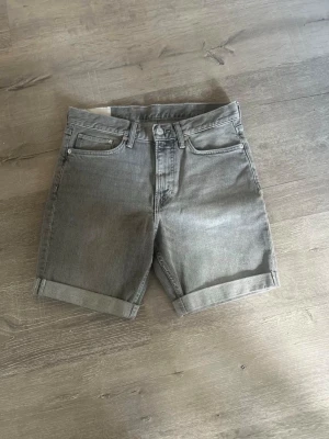 Grå jeansshorts med upprullad kant - Snygga grå jeansshorts med upprullad kant och klassisk femficksdesign. Perfekta för varma dagar och har en enkel, stilren look som passar till det mesta. Gjorda i ett slitstarkt bomullsmaterial.