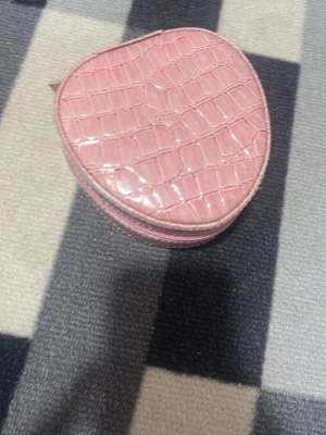 Rosa hjärtformad nesescär  - Söt hjärtformad plånbok i glansigt rosa material med krokodilpräglat mönster. Plånboken har dragkedja runtom och är perfekt för småsaker eller mynt. Trendig accessoar som sticker ut i väskan.