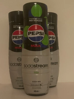 Sodastream Pepsi Max Lime Soda Mix - Tre flaskor Sodastream Pepsi Max Lime Soda Mix, 440 ml per flaska. Flaskorna är vita och svarta med gröna och röda detaljer. Används för att smaksätta kolsyrat vatten och ger upp till 9 liter dryck per flaska.