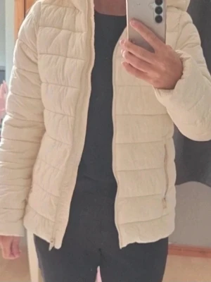 Beige pufferjacka med huva. Champion - Jacka i Strl M Sitter på mig som är S. Jag kan inte se några fläckar eller hål, mer än att texten börjat försvinna lite i jackan som syns på bild annars ser fin ut. Cremefärgad