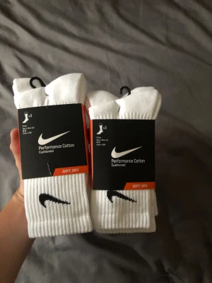 Vita Nike Performance strumpor 6-pack  - Säljer två paket Nike Performance Cotton strumpor i vitt, 3-pack per paket. Strumporna har svart Nike-logga, ribbad kant och är tillverkade i mjuk bomullsblandning för extra komfort. Perfekta till sneakers och vardagsstil.