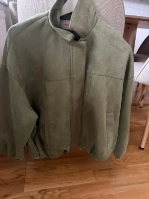 Grön mockajacka från Nelly - Snygg grön mockajacka från Nelly i storlek XXS. Jackan har hög krage, dragkedja framtill och två fickor. Materialet är mjukt och ger en exklusiv känsla. Perfekt för dig som vill ha en stilren och trendig jacka.