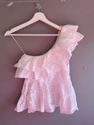 Vit oneshoulder topp med volang - Söt vit topp med oneshoulder-design och bred volangkant. Toppen har broderade detaljer och tunna axelband. Perfekt för sommarens varma dagar och ger en romantisk vibe till din outfit. Sååå söt verkligen!! Köpt här på plick men jag har aldrig använt den!💕