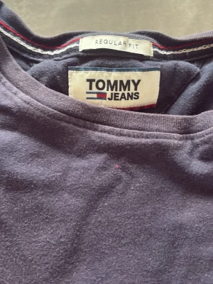 Mörkblå t-shirt från Tommy Jeans - Säljer en mörkblå t-shirt från Tommy Jeans med klassisk rund hals och liten broderad logga på bröstet. Modellen är regular fit och tillverkad i mjuk bomull. Perfekt basplagg för en clean och enkel stil. 