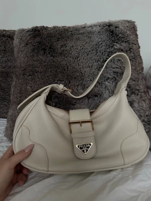 Beige väska - En krämvit/ ljusbbeige färg med guldfärgade detaljer, köpt secondhand 