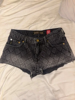 Mönstrade denimshorts från Superdry - Snygga gråsvarta denimshorts från Superdry med rå kant och coolt mönster över hela tyget. Klassisk femficksmodell med knappar och dragkedja framtill🙌🤩