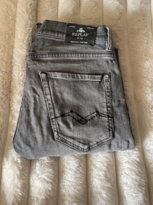 Grå jeans från Replay - Snygga grå jeans från Replay med klassisk femficksdesign och diskret logga på myntfickan. Jeansen har raka ben och är tillverkade i mjukt denimtyg som ger en avslappnad look. Perfekta för dig som gillar stilrena och tidlösa plagg.