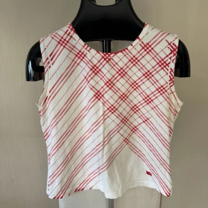 Burberry Vit och röd rutig linnetopp - Säljer en ärmlös linnetopp i vitt med röda rutiga linjer framtill. Toppen har rund halsringning och är croppad i modellen. Perfekt för dig som gillar en enkel men ändå unik stil.0379