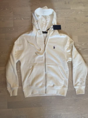 Vit hoodie från Polo Ralph Lauren - Tja! Säljer en helt ny Snygg vit zip hoodie från Ralph Lauren.                                                                                  Storlek är medium och måtten finns på sista bilderna.                                                                                   Den är helt ny så aldrig använd bara testad.                     Priset kan diskuteras och skickar inom 24 Tim ☺️💨