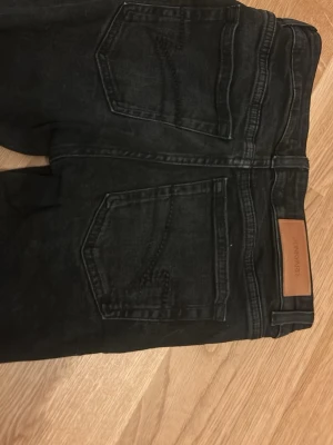 Svarta bootcut jeans från junkyard - Säljer ett par svarta bootcut jeans från junkyard. Jeansen har klassisk femficksdesign, silverfärgade knappar och en snygg tvättad look. Materialet är stretchigt och bekvämt, perfekt för en trendig vardagsstil.