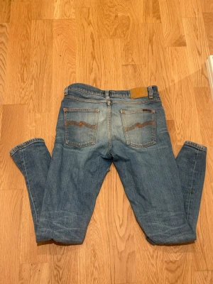 Nudie jeans lean dean - Snygga blå jeans i klassisk modell med fem fickor och ljusa slitningar. Jeansen har raka ben och detaljerade bakfickor med broderad söm. Perfekta för en avslappnad och trendig look. Dem har även en defekt som man ser i bild 3 men när man har på sig dem så syns de knappt.