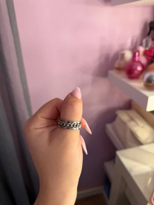 Silvrig unisex ring med kedja  - Helt oanvänd silverfärgad unisex ring med kedjedetalj 🤍⛓️ Stilren och unik ring med dekorativ kedja på ett silverfärgat band av rostfritt stål. Kedjan går att snurra på, vilket ger ringen en lite annorlunda och cool detalj.  Passar perfekt till vardags eller som statement-smycke.  Storlek 10