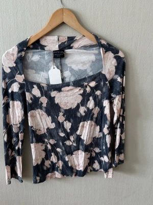 Trussardi Blommig långärmad topp med öppen rygg - Supersnygg långärmad topp från Trussardi med blommigt mönster i ljusrosa och mörkblå toner. Toppen har en fyrkantig ringning och en cool öppen detalj i ryggen. Perfekt för dig som vill sticka ut lite extra med din outfit. 0053