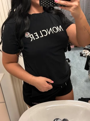 Svart Moncler t-shirt med logga - Säljer en svart t-shirt från Moncler med vit logga och emblem på bröstet. Klassisk passform och rund halsringning. Perfekt till jeans eller shorts för en clean och stilren look.